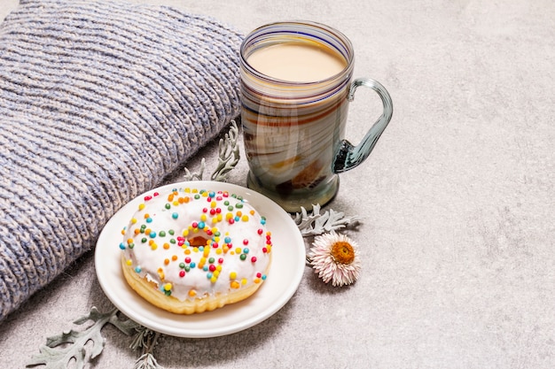 Café caliente con una rosquilla. Bebida de invierno para un buen humor con suéter, hojas y flores.