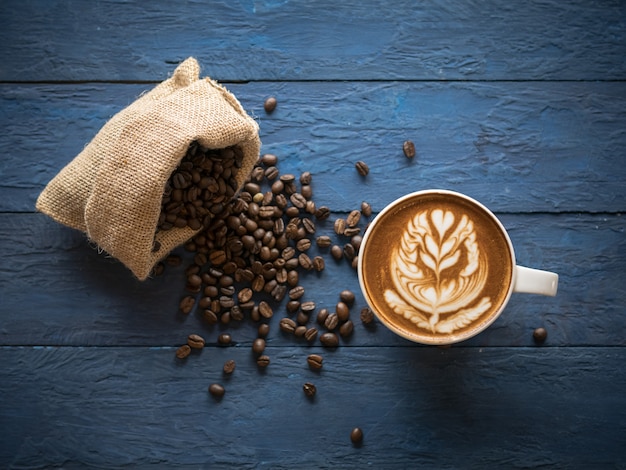 Café caliente en una taza con bello arte latte y granos de café