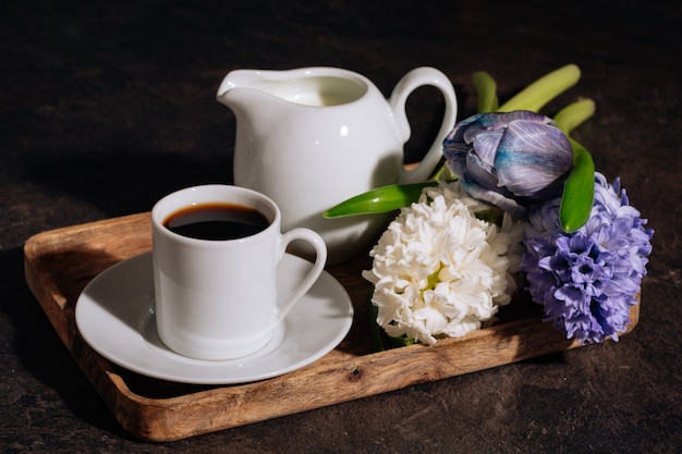 Café caliente en taza blanca con leche y flores de jacinto en bandeja de madera