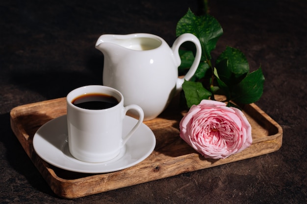 Café caliente en taza blanca con leche y flores rosa rosa en bandeja de madera