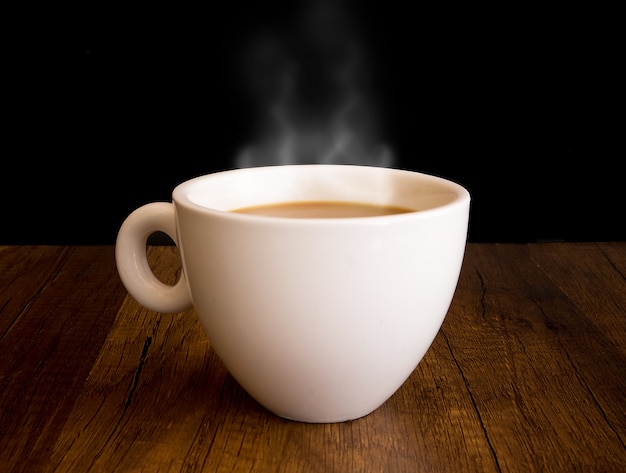 Café caliente con vapor de una taza, en la mesa de madera y fondo negro