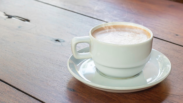 Café caliente en vaso blanco sobre mesa de madera.