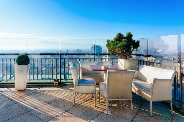 Café callejero vacío con mesas y sillas y hermoso fondo panorámico en la ciudad vieja de Ljubljana, capital matutina de Eslovenia. Diseño de restaurante moderno con lámparas en ciudad soleada, amanecer en invierno