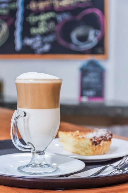 Foto café cappuccino e um pedaço de bolo em uma bandeja de servir de restaurante.