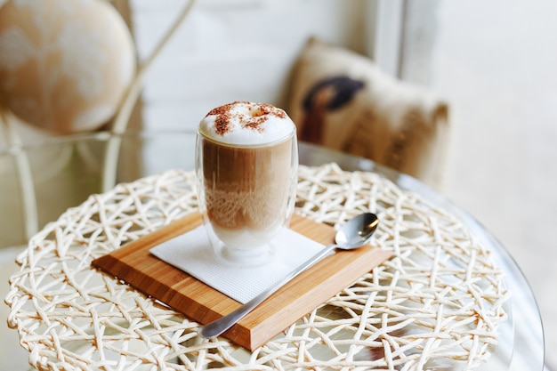 Café cappuccino na mesa no café. Café com leite com leite e chocolate por cima no copo na travessa com colher.