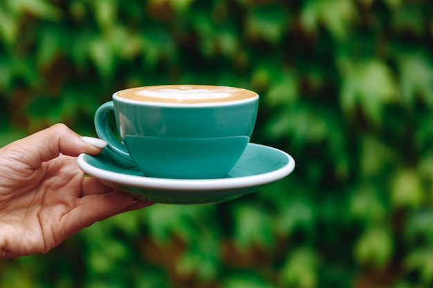 Café capuchino aromático caliente con arte latte en una taza de color turquesa