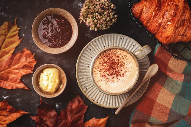 Café capuchino con croissant en la mesa, concepto de desayuno de otoño, vista superior