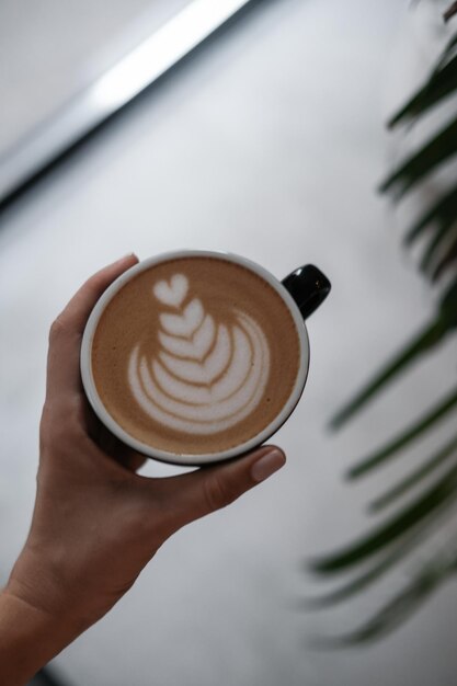 Foto café capuchino en la mano de una mujer desde arriba