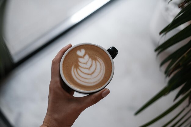 Foto café capuchino en la mano de una mujer desde arriba