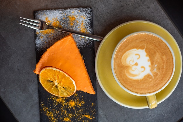 Café capuchino en taza amarilla con tarta de queso en café