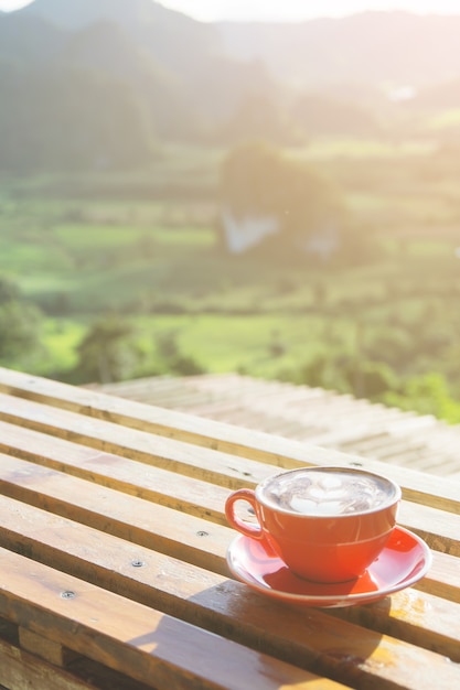 Foto el café capuchino en una taza roja puso sobre la mesa de madera