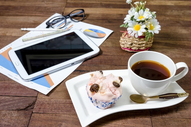 café com bolo de xícara vaporizado e equipamentos de escritório na mesa de trabalho