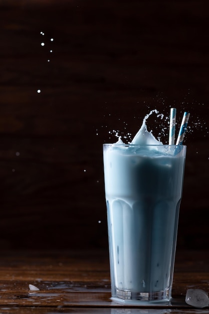Café com leite azul em um copo de vidro alto com dois canudos O spray está voando
