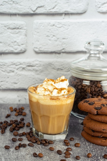 Café com leite caramelo em copo com chantilly e biscoito de chocolate. Grãos de café na superfície da parede de tijolo cinza e branco com espaço de cópia.