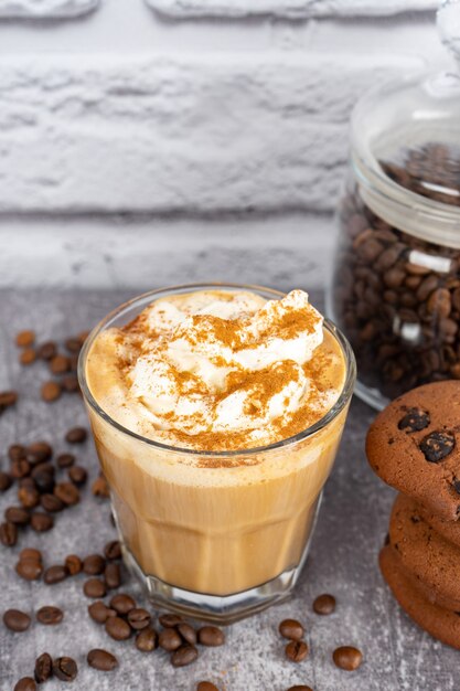 Café com leite caramelo em copo com chantilly e biscoito de chocolate. Grãos de café na superfície da parede de tijolo cinza e branco com espaço de cópia.
