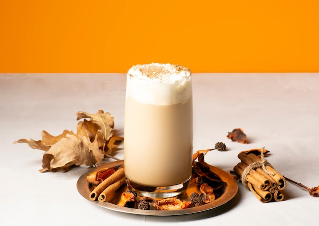 Café com leite de abóbora de outono tradicional em um copo em uma bandeja de metal com especiarias.