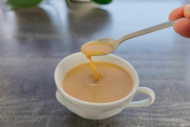 Café com leite em uma caneca branca A mão mexe o café com uma colher Uma gota de café cai em uma caneca