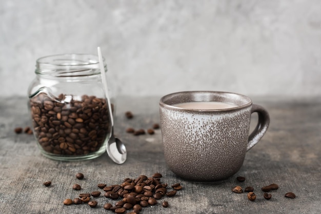 Café com leite em uma xícara de cerâmica e jarra com grãos de café na mesa Tempo para uma pausa e relaxamento