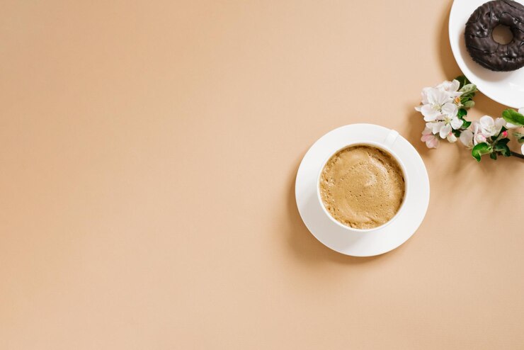 Café com leite em uma xícara de porcelana branca e rosquinhas de chocolate com flores de maçã branca sobre um fundo bege O conceito de café da manhã ou pausa para café