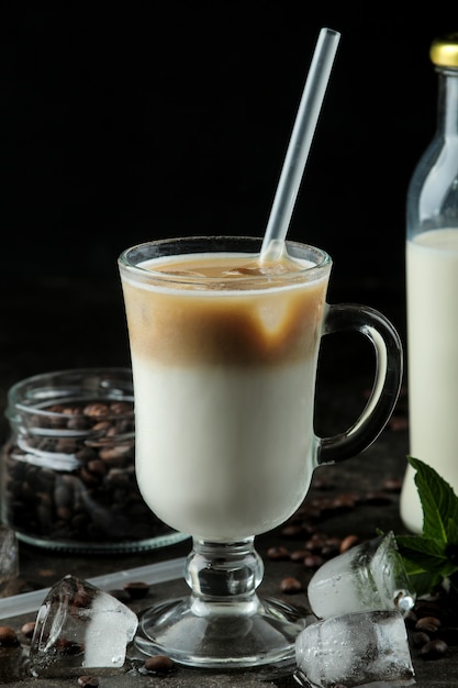 Café com leite gelado ou café gelado com leite e cubos de gelo em um copo de vidro contra um fundo escuro. bebida refrescante. bebida de verão.