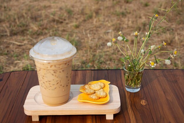 Café com leite ou mocha ou cappuccino gelado serve com biscoito de pão e flor de grama na mesa de madeira para viajantes tailandeses descansam relaxam comer e beber ao lado do canal de irrigação em Nonthaburi Tailândia