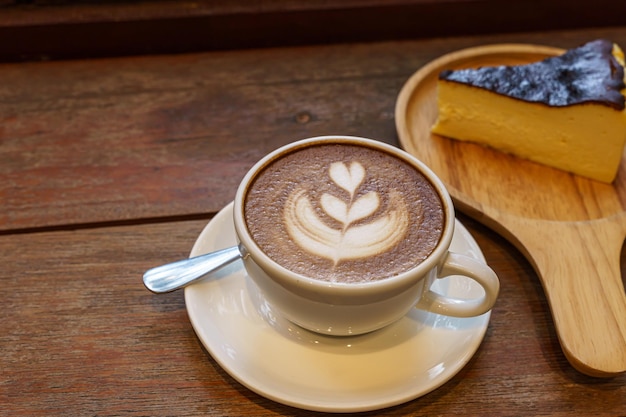 Café com leite quente com espuma de leite latte art na caneca do copo e mesa de madeira de bolo de chocolate caseiro na mesa de madeira na vista superior como café da manhã em uma cafeteria no conceito de trabalho de negócios de café