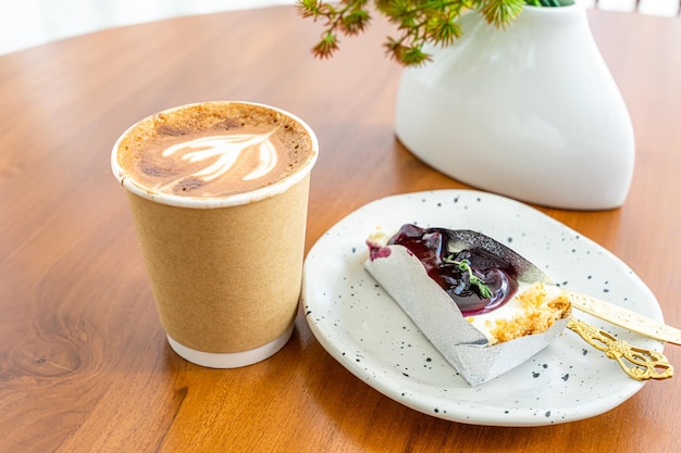 Café com leite quente com espuma de leite latte art no copo feito de papel e bolo de mirtilo na mesa de madeira na vista superior como café da manhã em uma cafeteria no conceito de trabalho de negócios de cafedura