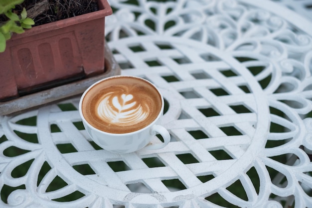Café com leite quente com forma de flor em copo branco na mesa retrô