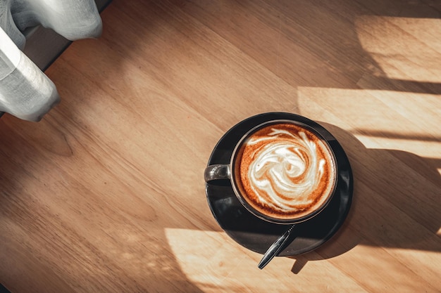 Café com leite quente com latte art na forma de espuma de leite na caneca do copo na mesa de madeira na vista superior como café da manhã em uma cafeteria no conceito de trabalho de negócios de cafedura