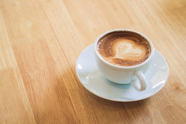 Café com leite quente em forma de coração em uma caneca branca colocada em um piso de madeira Copiar espaço