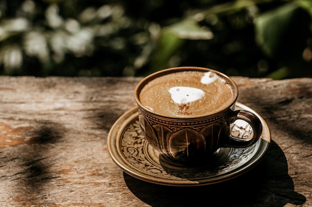 Café com leite quente em uma xícara sobre uma mesa de madeira vintage.