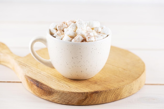 Café com marshmallows e canela em uma caneca em uma placa de madeira