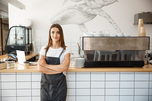 Café conceito do empresário - retrato de atraente e atraente barista caucasiano bonito no avental sorrindo na câmera no balcão do café.