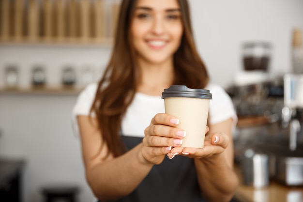 Café concepto de negocio - Hermosa dama del Cáucaso sonriendo a la cámara ofrece desechables llevar el café caliente en la cafetería moderna