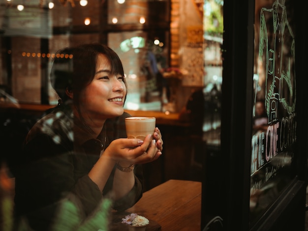 Café de consumición de la mujer asiática en café de la cafetería