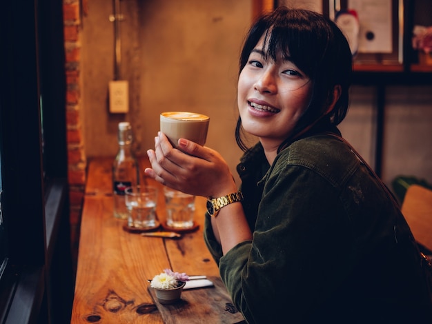 Café de consumición de la mujer asiática en café de la cafetería