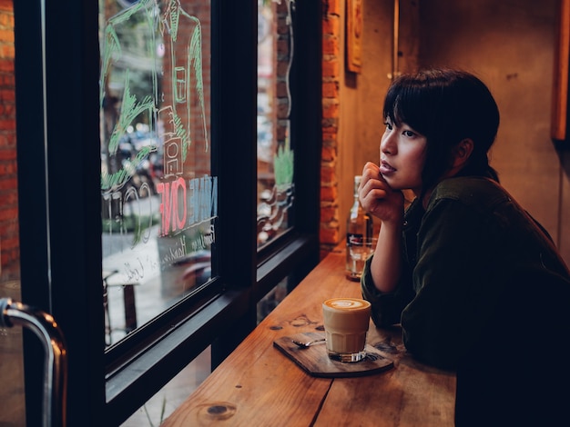 Café de consumición de la mujer asiática en café de la cafetería