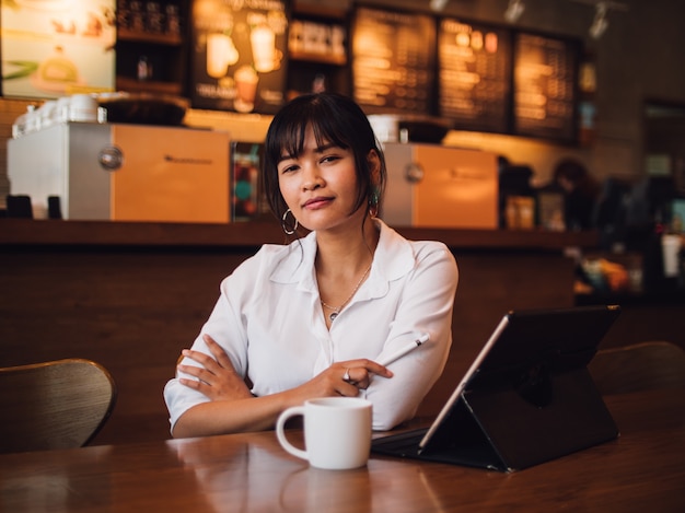 Café de consumición de la mujer asiática en café y usar el ordenador portátil para el negocio de trabajo
