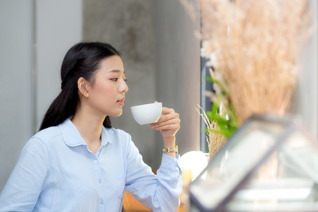 Café de consumición de la mujer asiática hermosa y sonrisa por la mañana en el café.