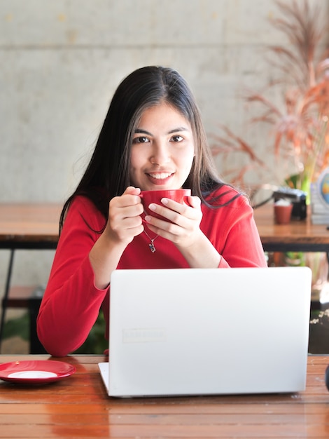 El café de consumición de la mujer asiática y se relaja en café de la cafetería