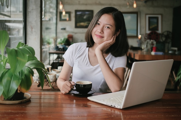 El café de consumición de la mujer asiática y se relaja en café de la cafetería