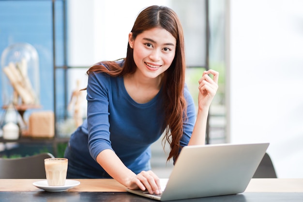 Café de consumición de la mujer asiática y trabajo con el ordenador portátil