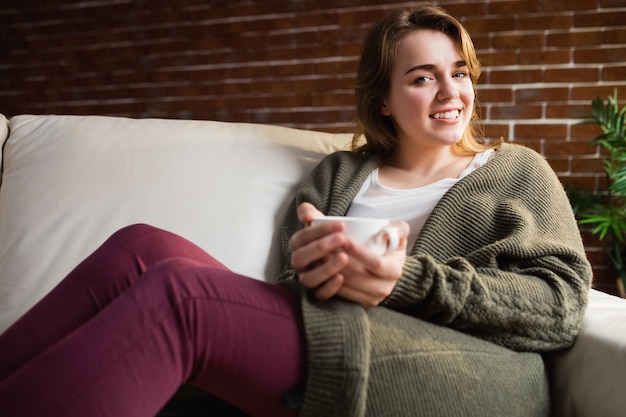 Café de consumición de la mujer bonita que miente en el sofá en la sala de estar