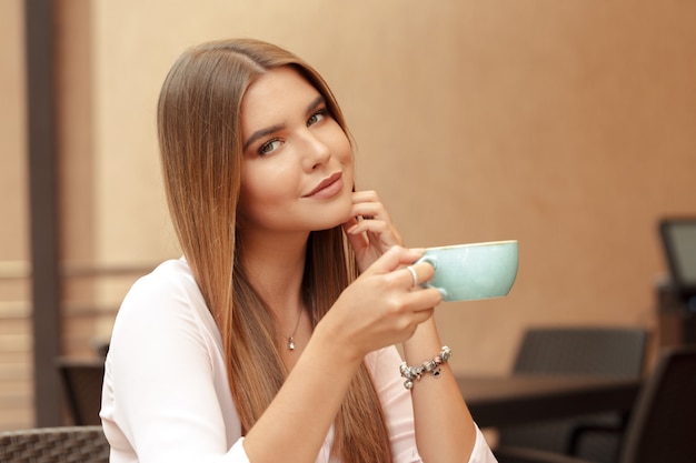 Café de consumición de la mujer joven en un café al aire libre