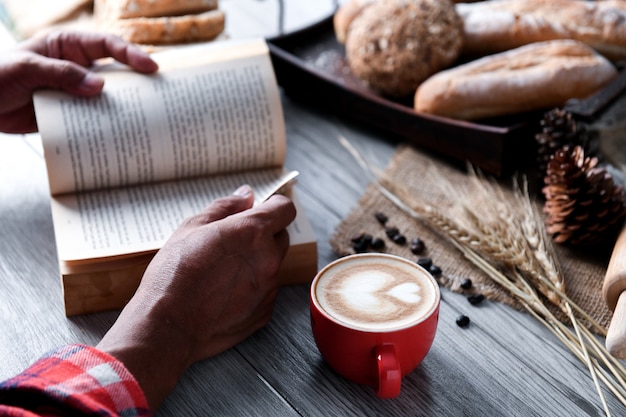 Café del corazón en taza roja con la gente que lee un libro.