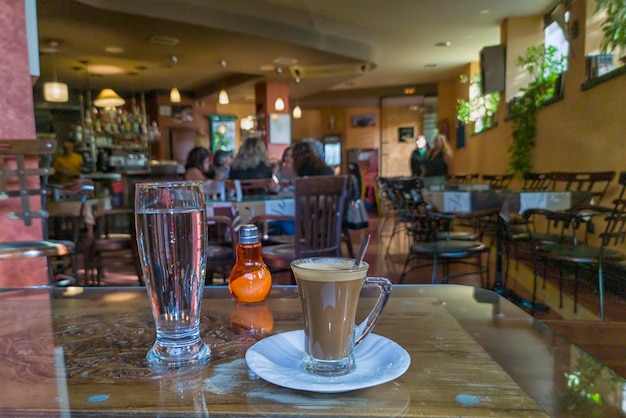 Café cortado con leche junto con un vaso de agua fresca