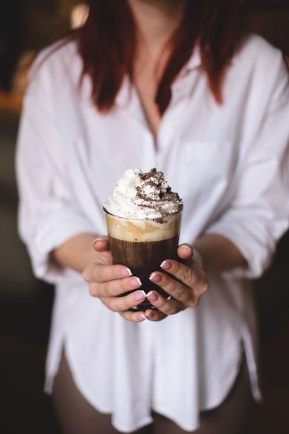 Café con crema batida y chispas de chocolate en manos de una chica