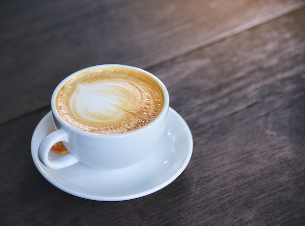 Café con crema en forma de corazón, taza blanca en la mesa de madera.