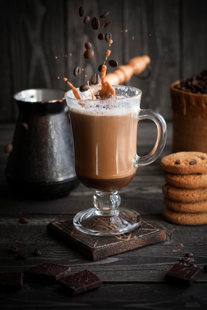 Café con crema con salpicaduras y granos en vuelo con galletas sobre un fondo oscuro de madera