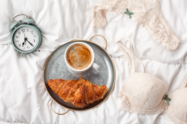 Café con croissant, despertador, ropa interior de niña.